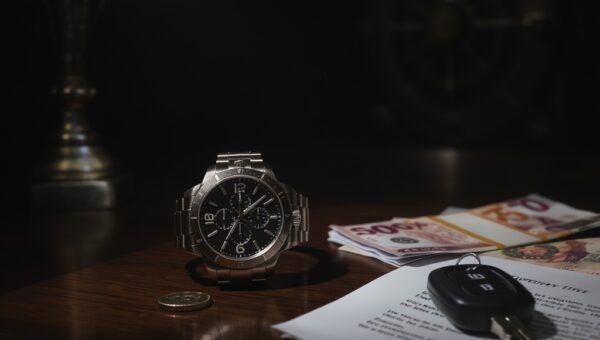 Luxury watch, coins, canadian money, and car keys on dark mahogany desk,